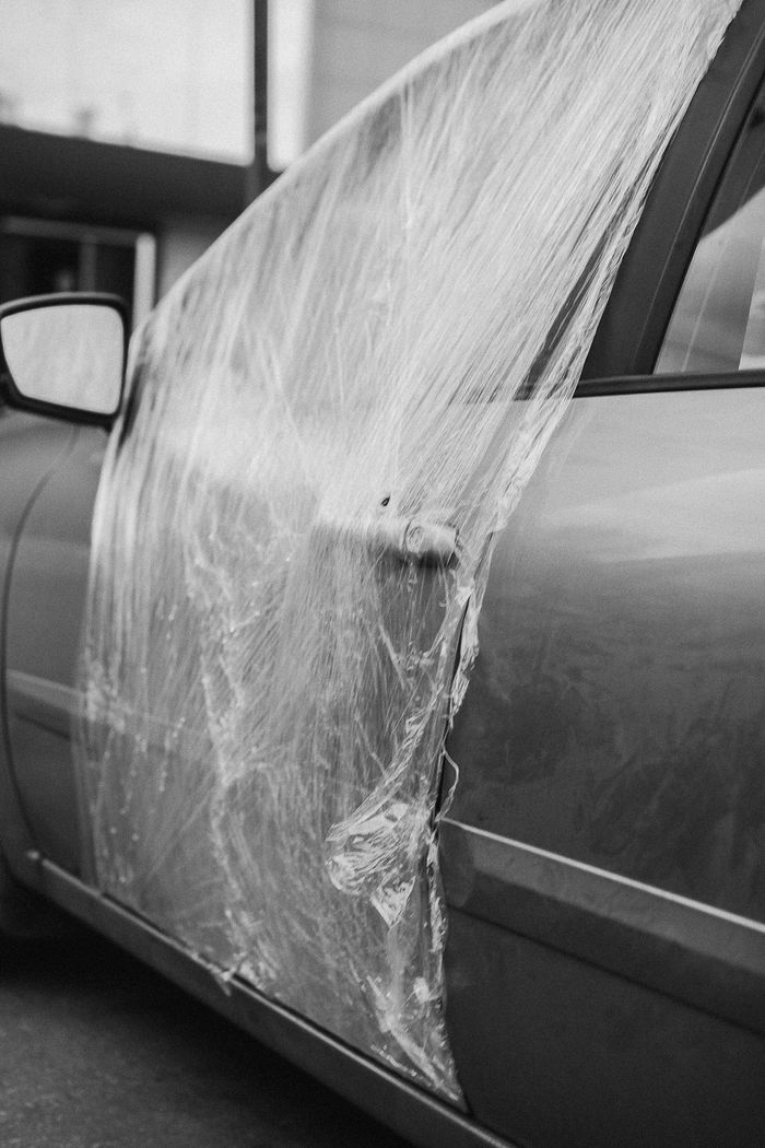 A grayscale image of a car door repaired with plastic wrap, showcasing temporary solutions.